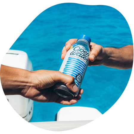 two hands holding an Open Water aluminum bottle by the sea